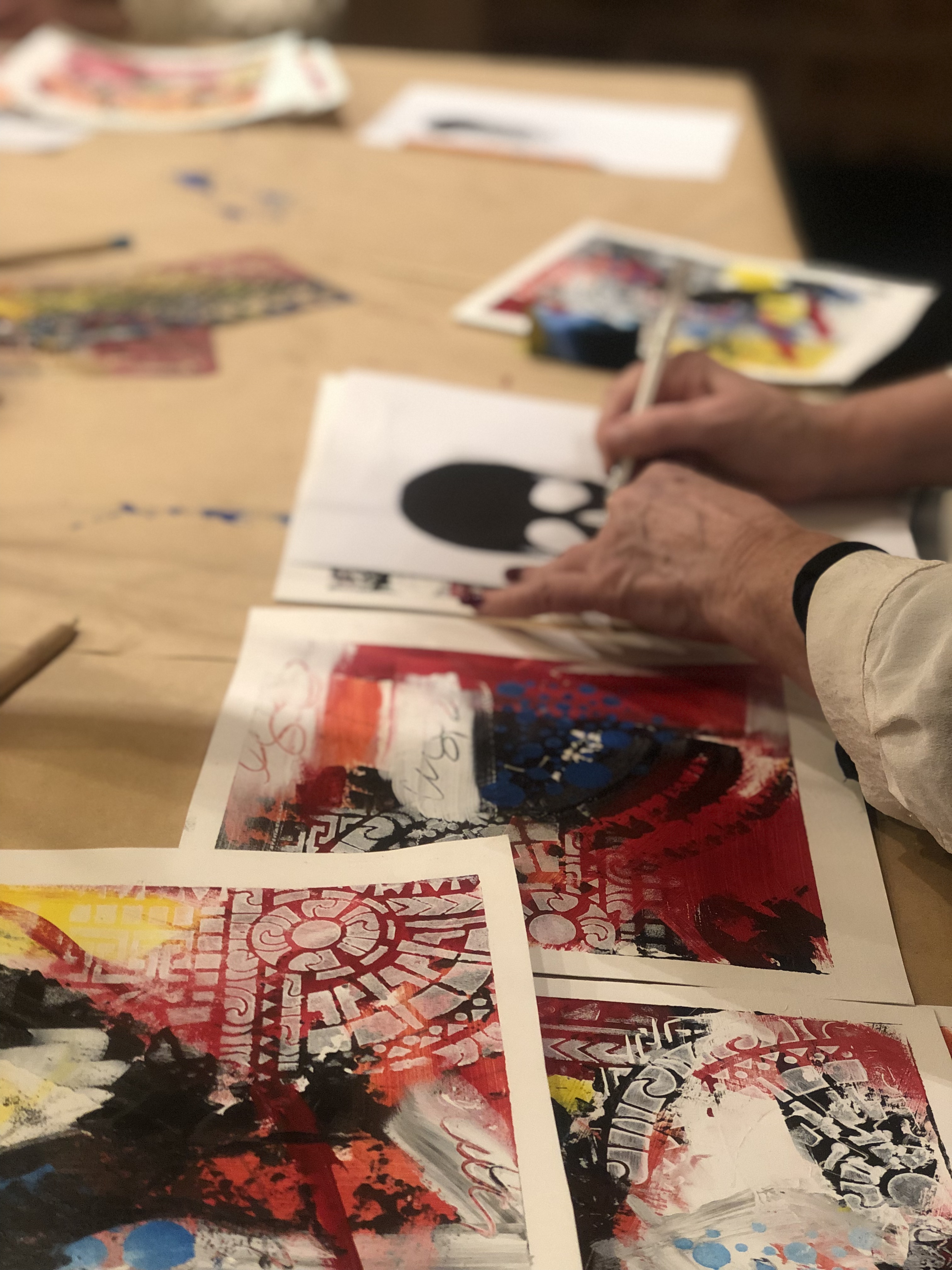 Completed paintings spread across the table at a Blanke ark til mesterverk session